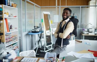 Young successful cross-armed fashion designer looking at you while working in studio